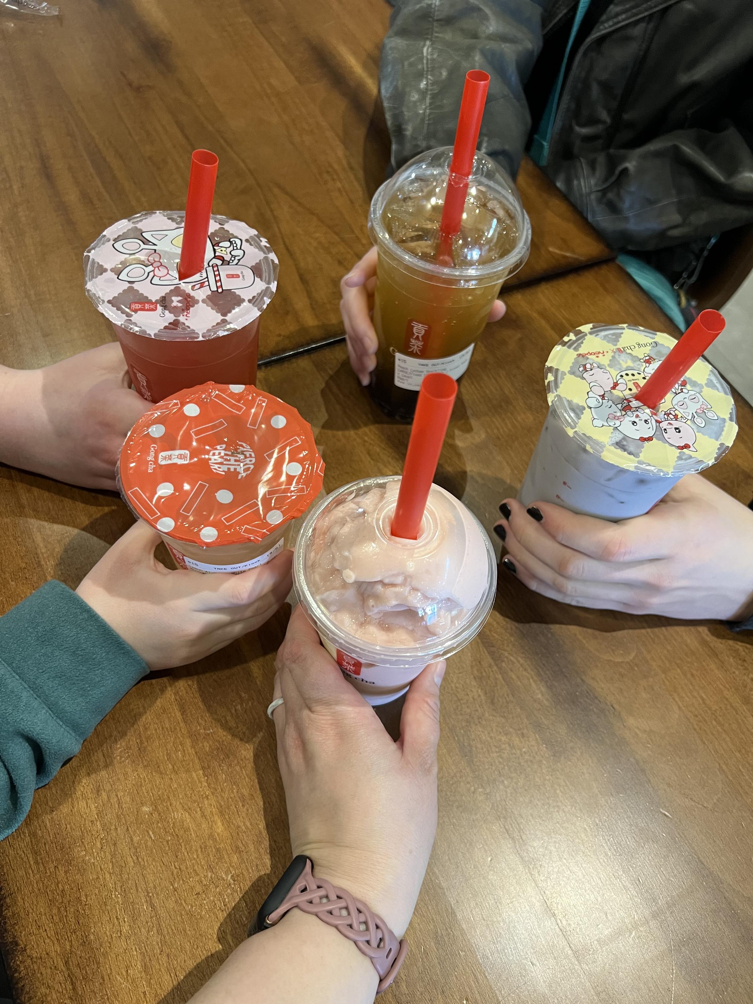 Five white hands holding boba style drinks all in the center of a table.
