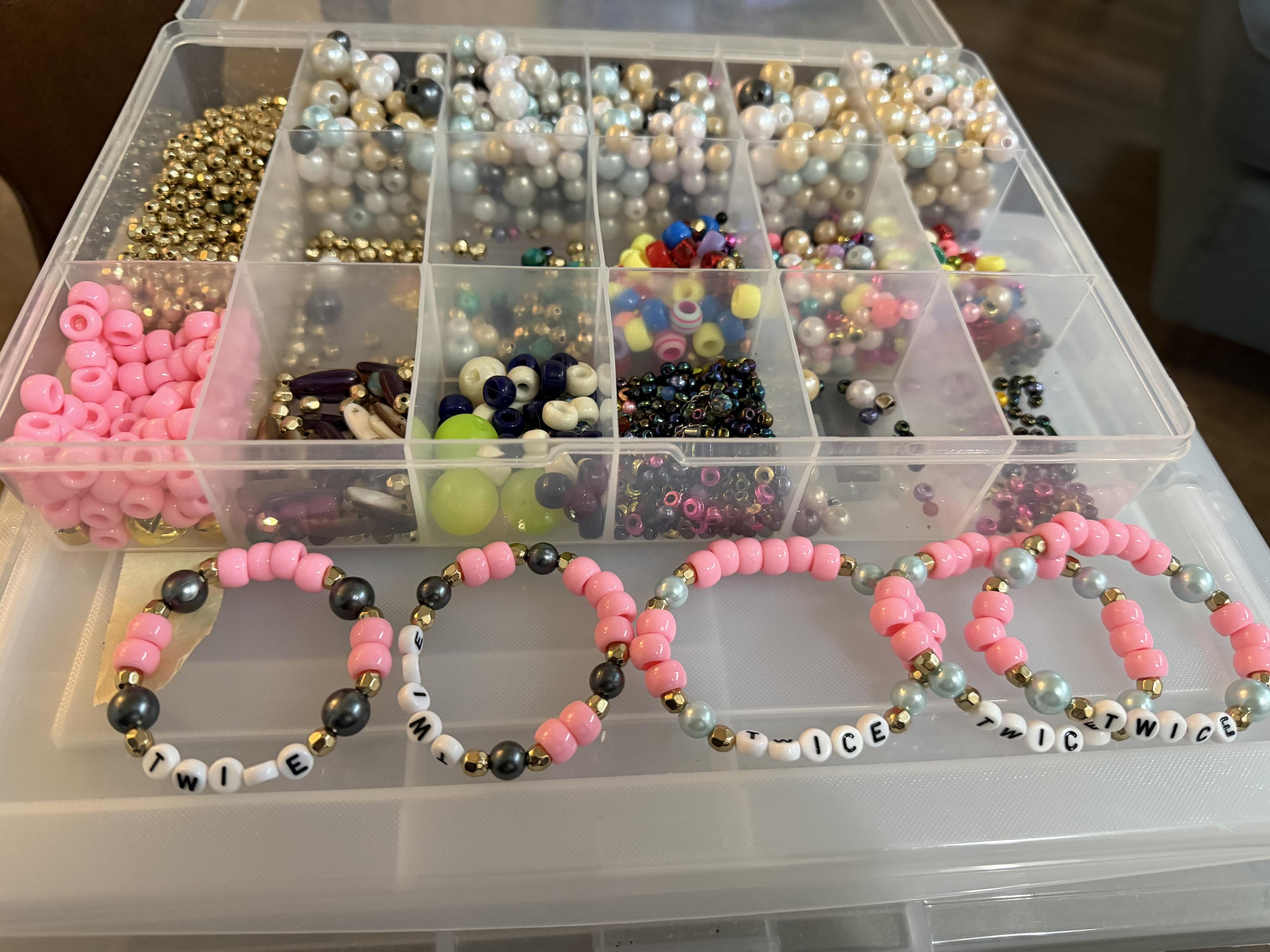 five pink and gold and blue bracelets lined up near a box of mixed beads. The brackets say Twice