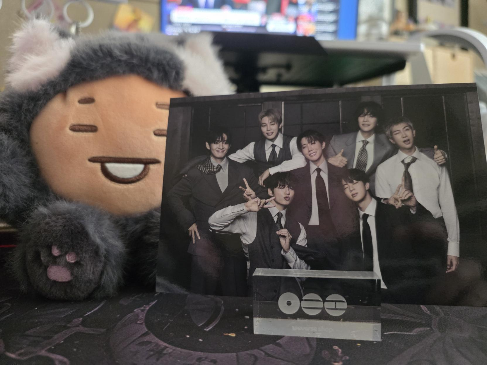 A photo of BTS on an Arirang themed stand, with a Shooky-Kitty plushie beside it, on my very messy desk.