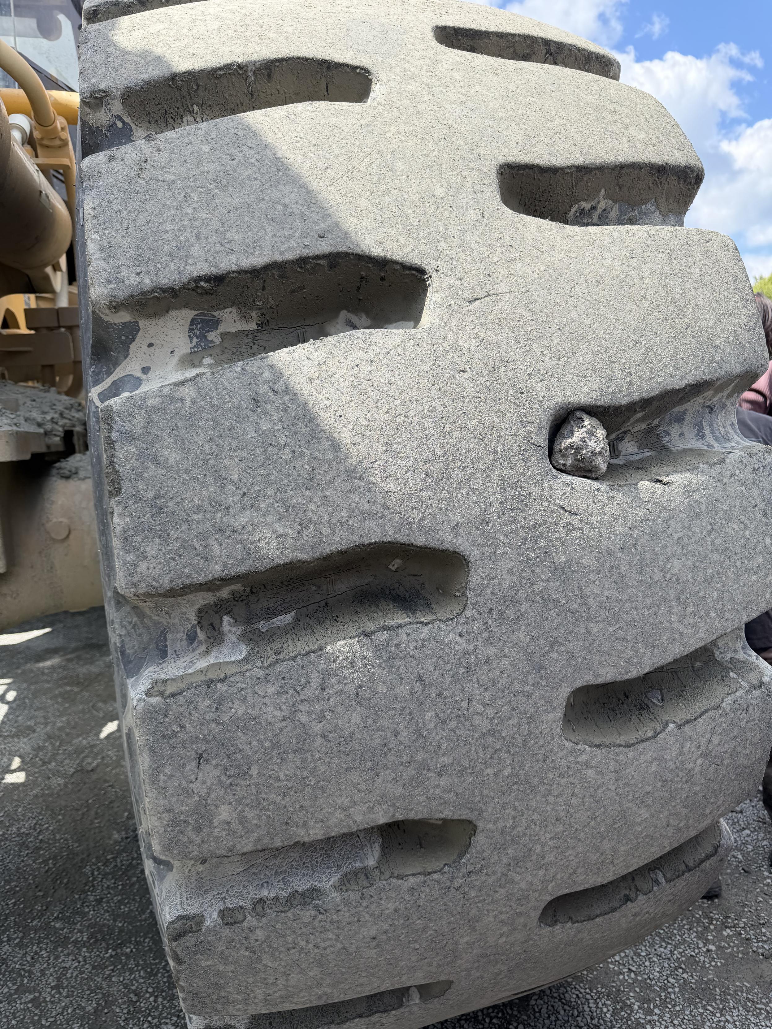 An adult fist size rock stuck in the groves in a tire as tall as an adult. The tire and the rock at the same dusty grey.
